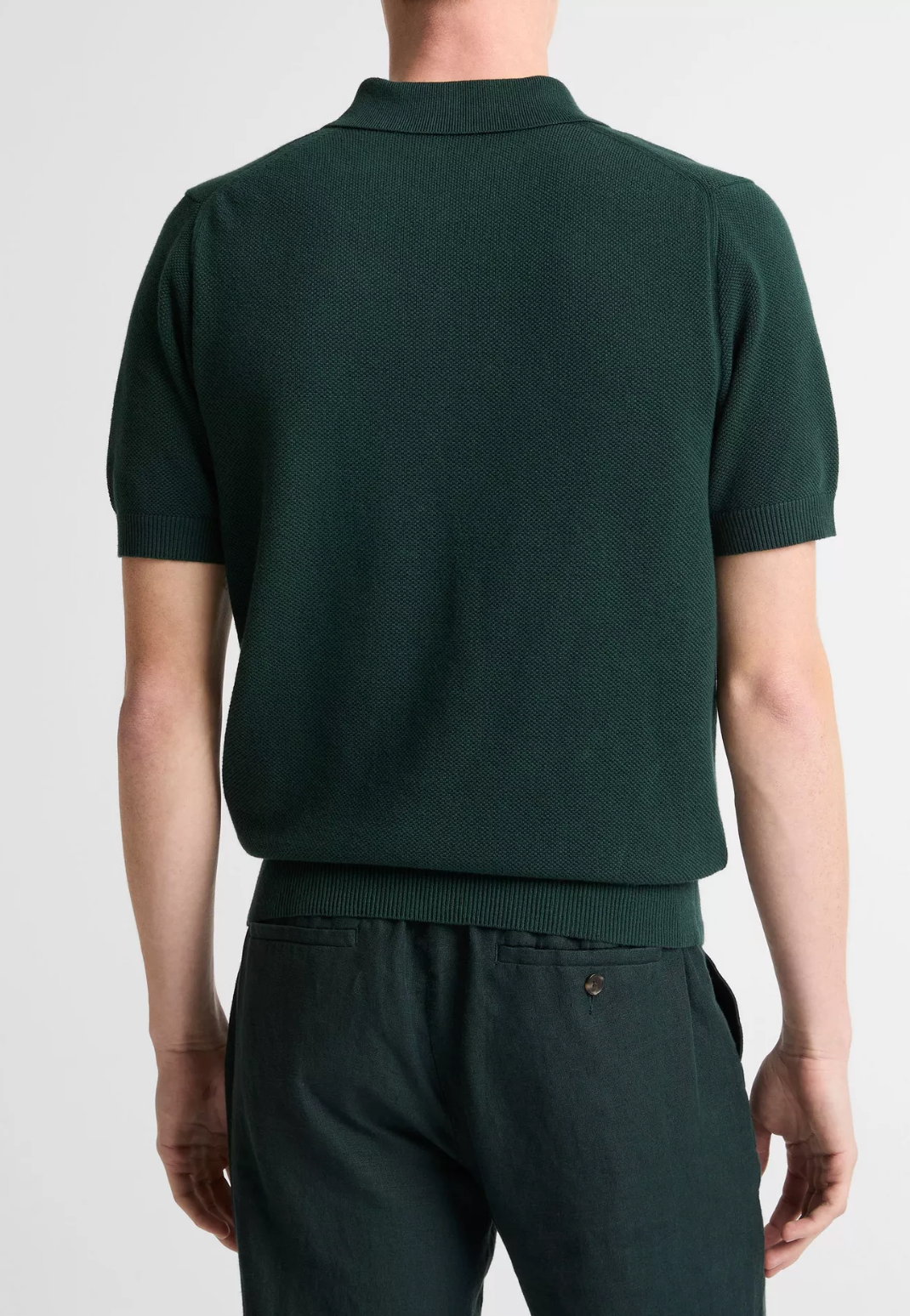 Back view of man wearing Vince short-sleeve zip polo shirt in dark green with ribbed collar and hem.