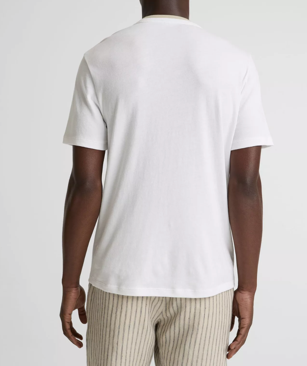 Back view of man wearing Vince white short-sleeve crew neck t-shirt with striped pants against neutral background.