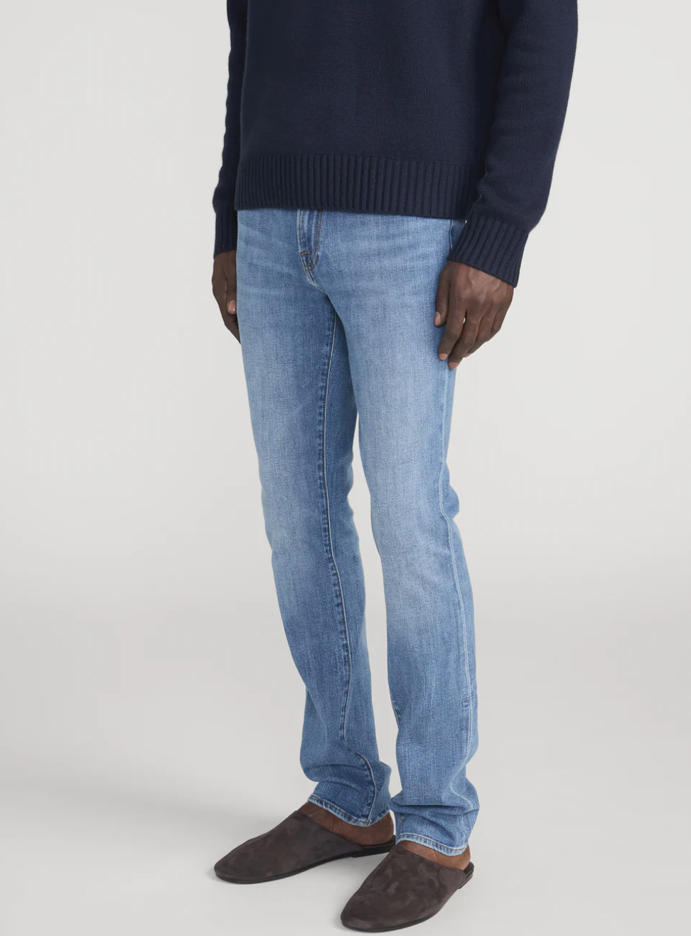 Frame L'Homme Slim jeans in light blue wash, shown on model wearing dark sweater and brown shoes.