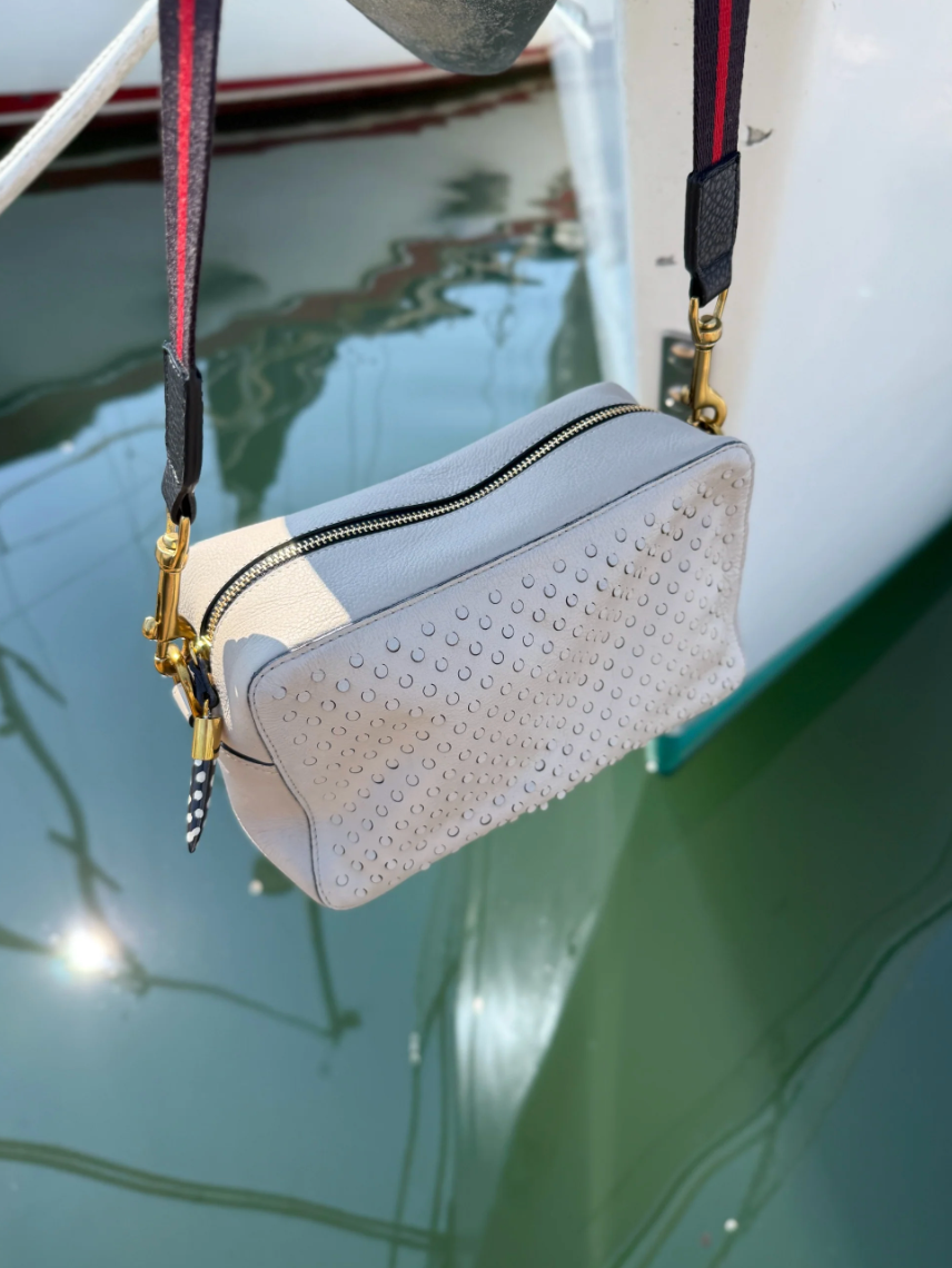 Kempton Amberleigh perforated leather crossbody bag with adjustable strap and gold hardware hanging over water