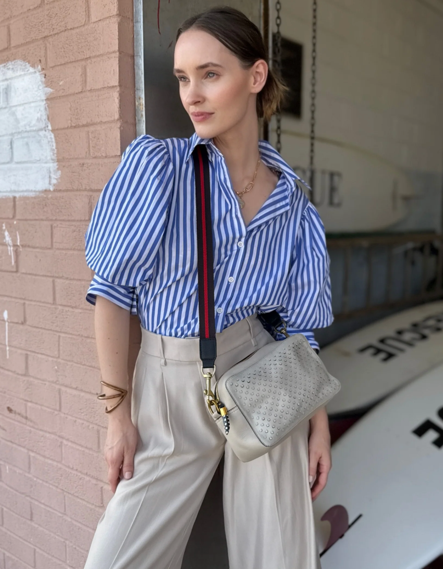 Woman wearing striped shirt carrying Kempton Amberleigh perforated leather crossbody bag with chain strap and studded deta...