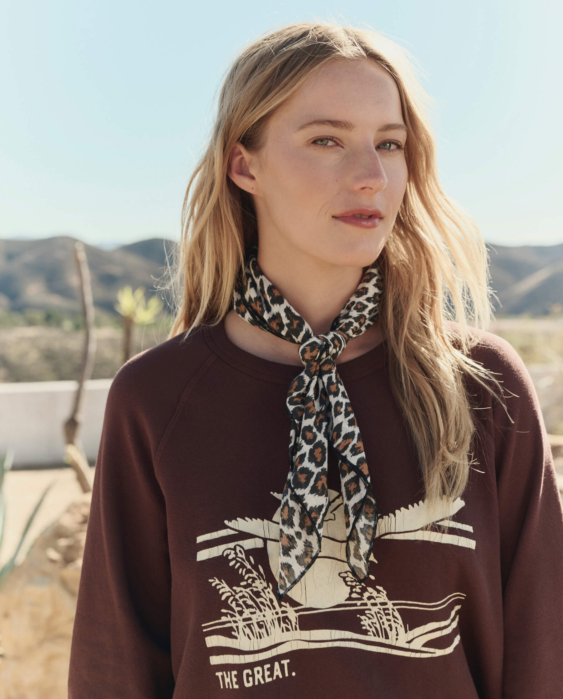 Model wearing leopard print bandana tied at neck over brown The GREAT sweatshirt in desert setting
