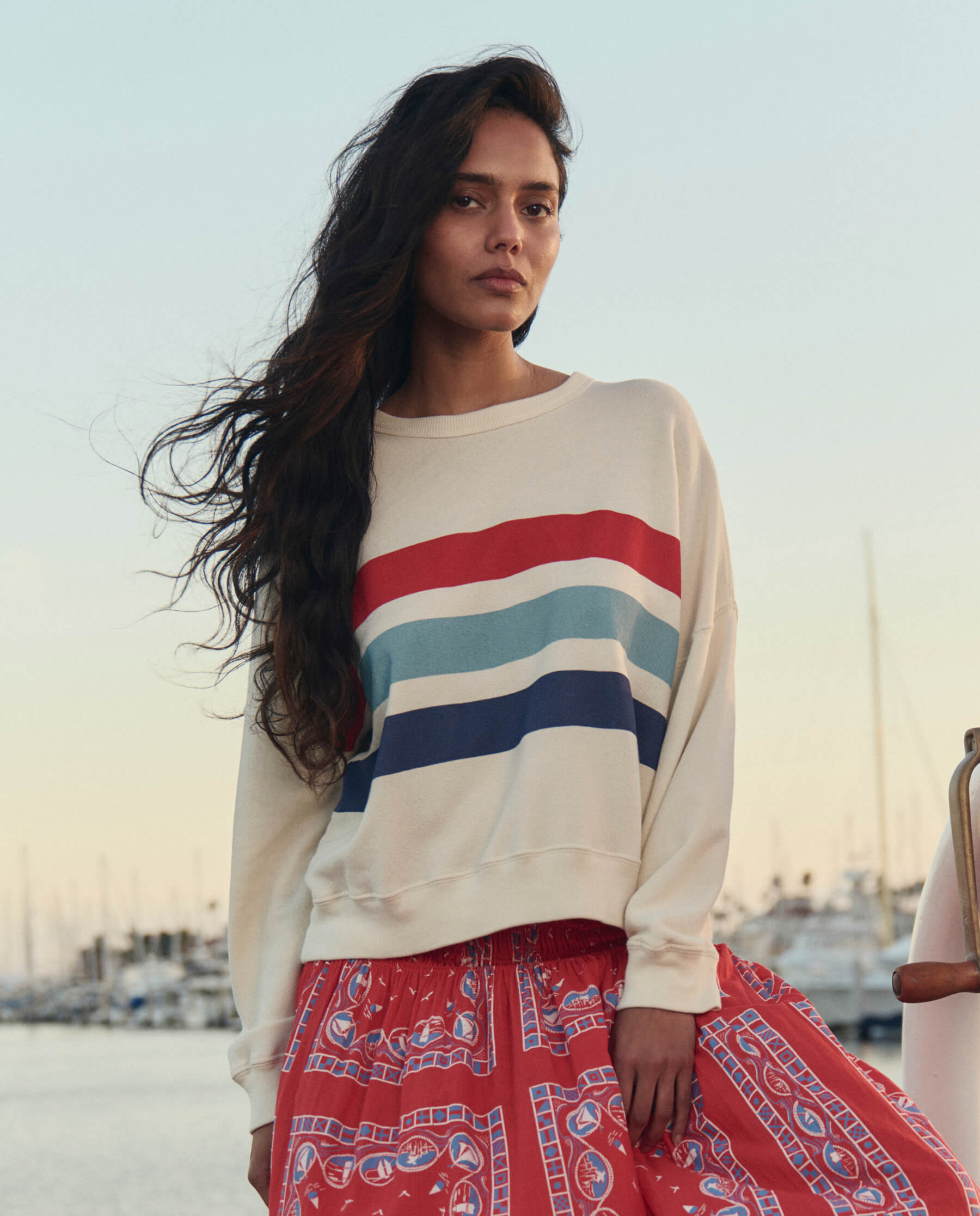 Woman wearing white sweatshirt with horizontal red, light blue and navy stripes in marina setting