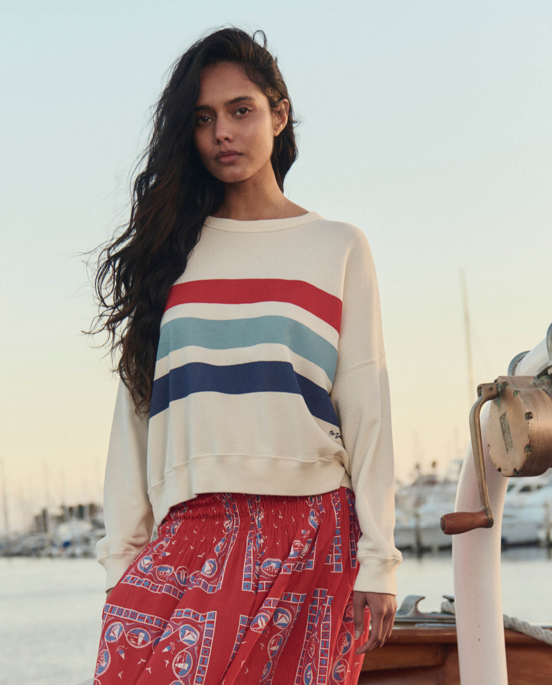 Woman wearing white sweatshirt with red light blue and navy horizontal stripes on boat