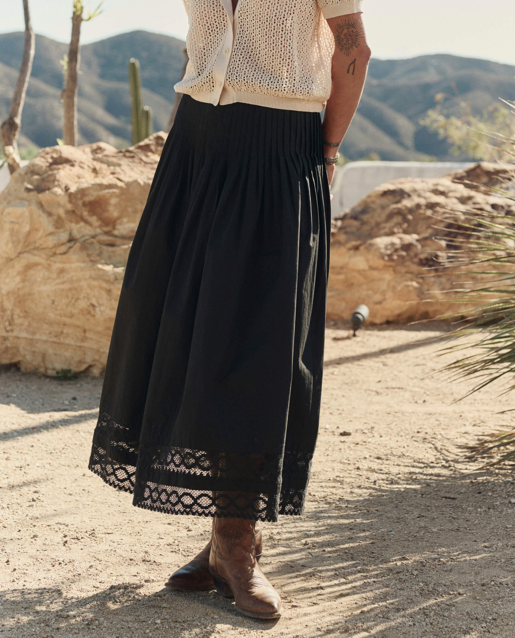 Model wearing black structured Victorian midi skirt with lace hem and cowboy boots in desert setting