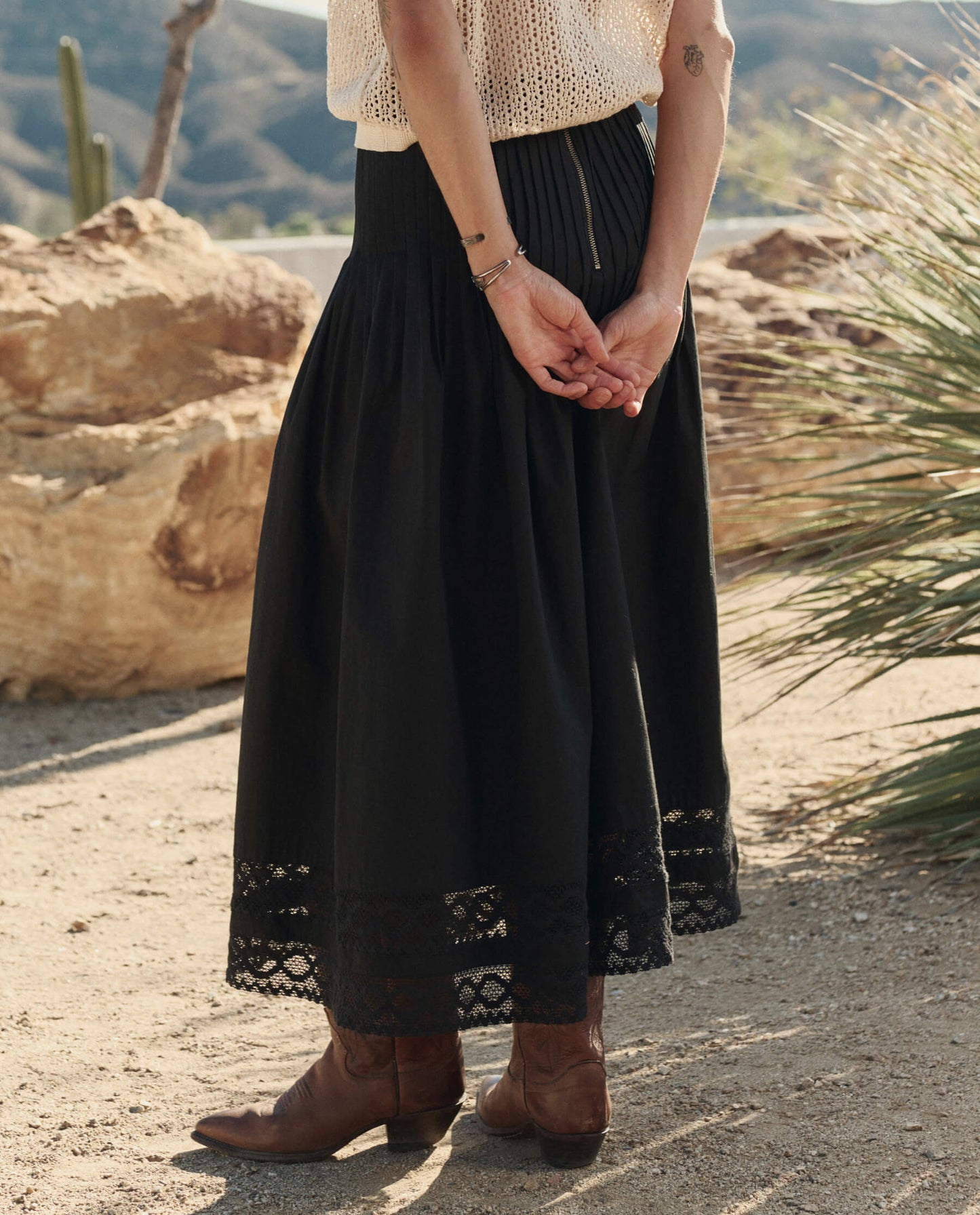 Model wearing black Victorian midi skirt with lace hem trim and brown cowboy boots in desert setting