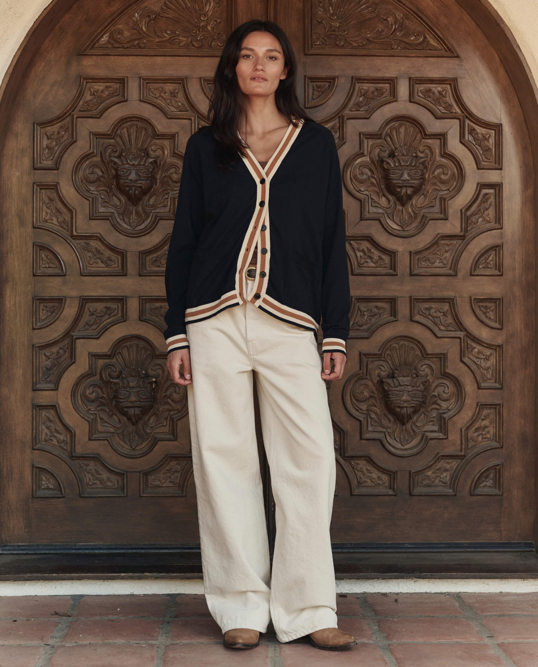 Model wearing black V-neck cardigan with cream and tan stripe trim, paired with wide-leg cream trousers