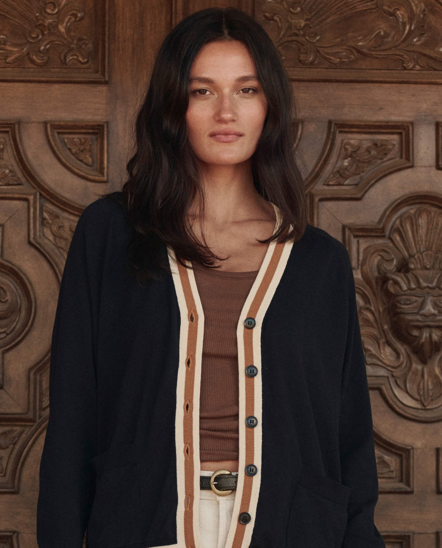 Model wearing The GREAT Bowery Cardigan in black with cream and tan stripe trim