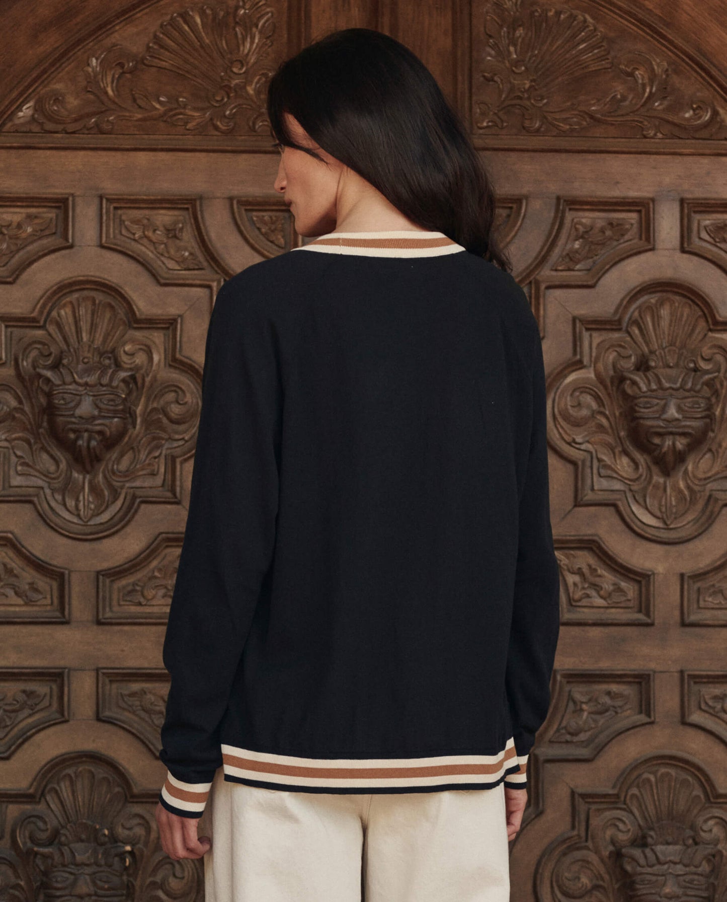 Back view of black cardigan with cream and tan stripe trim on model