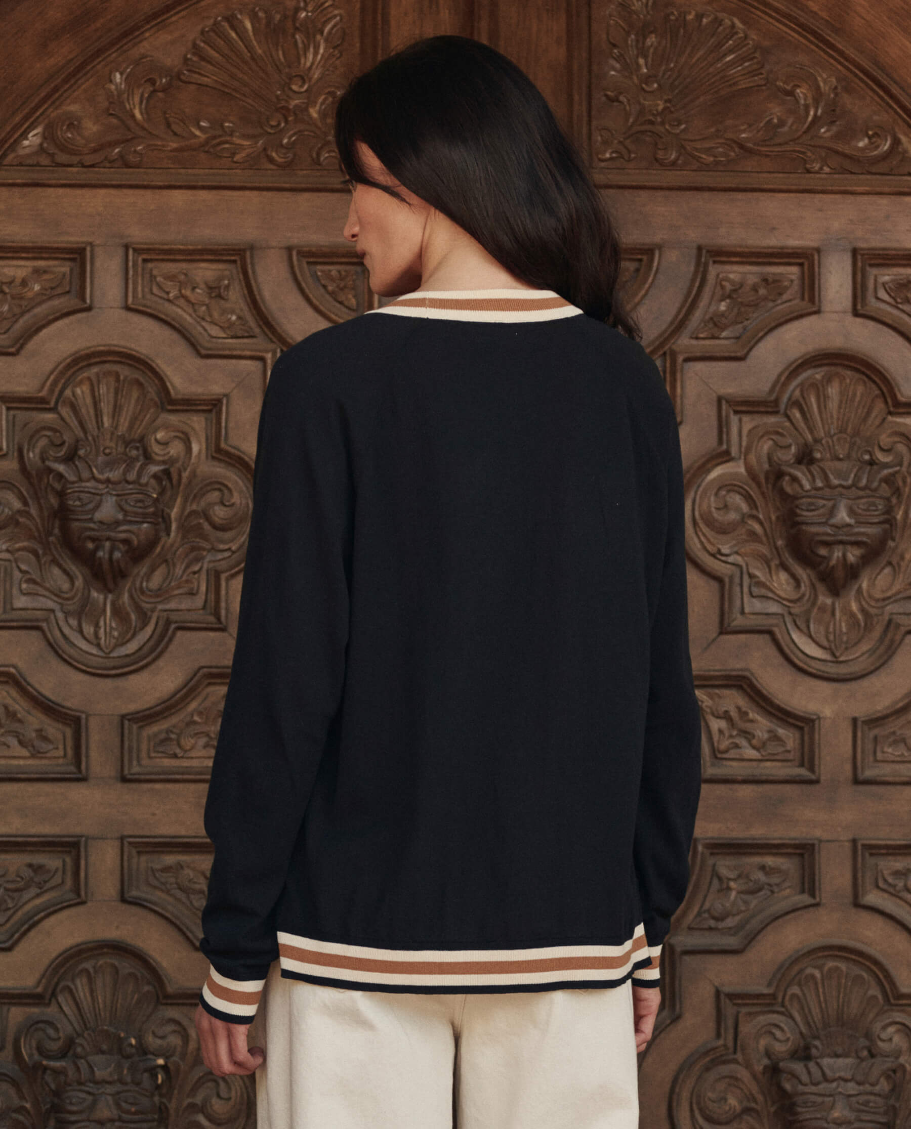 Back view of black cardigan with cream and tan stripe trim on model