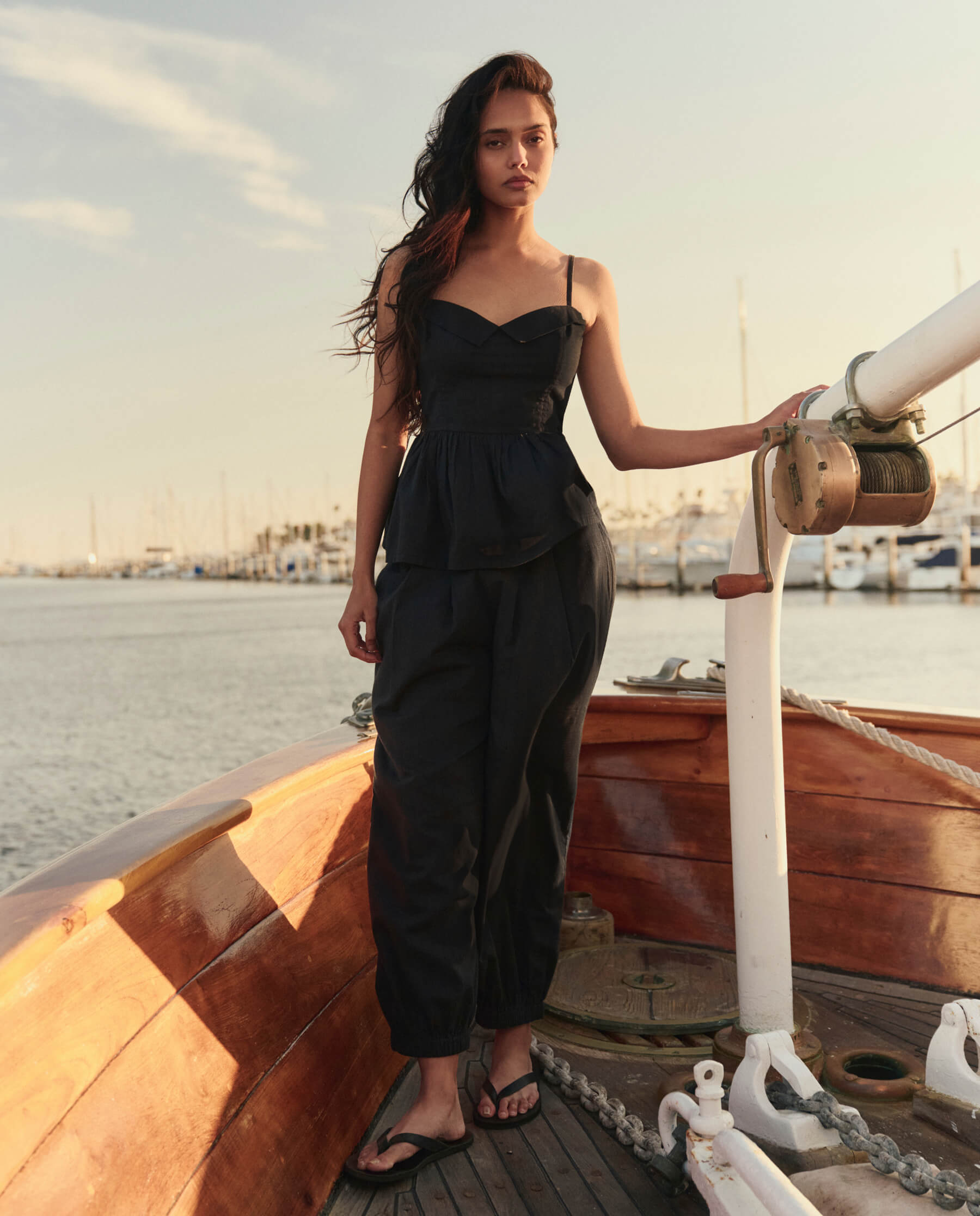 Model wearing black textured bustier-style top with spaghetti straps on a wooden sailboat