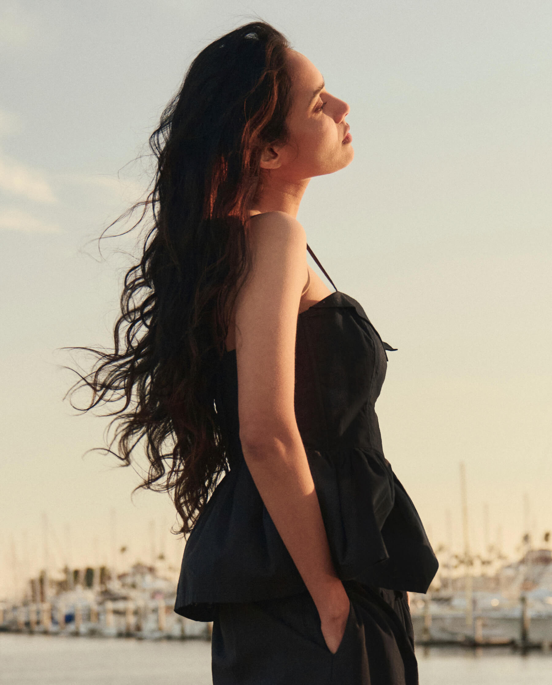 Model wearing black textured strapless verse top at golden hour near marina