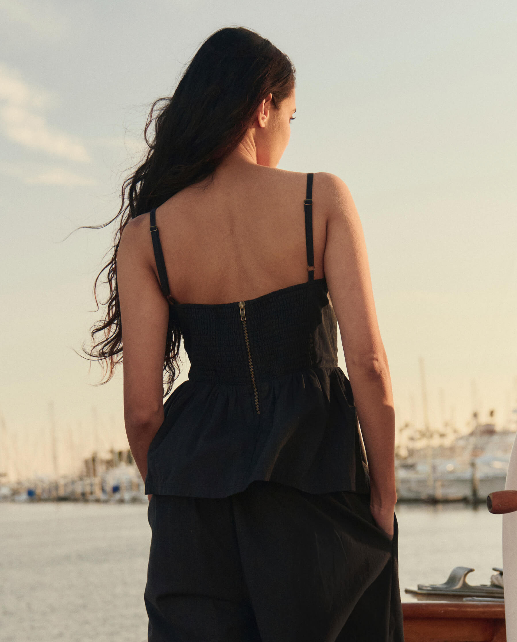 Woman wearing black textured peplum camisole top with back zipper detail near marina