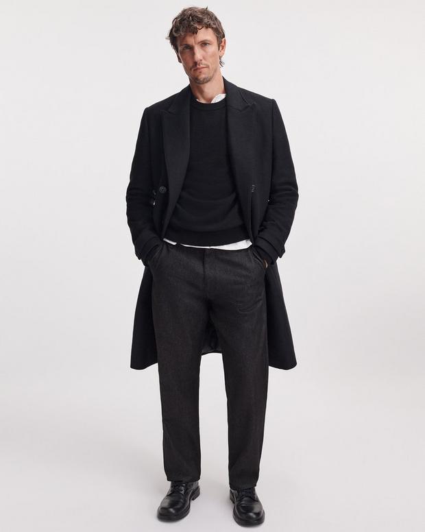 Male model wearing black cashmere crew neck sweater layered under black overcoat