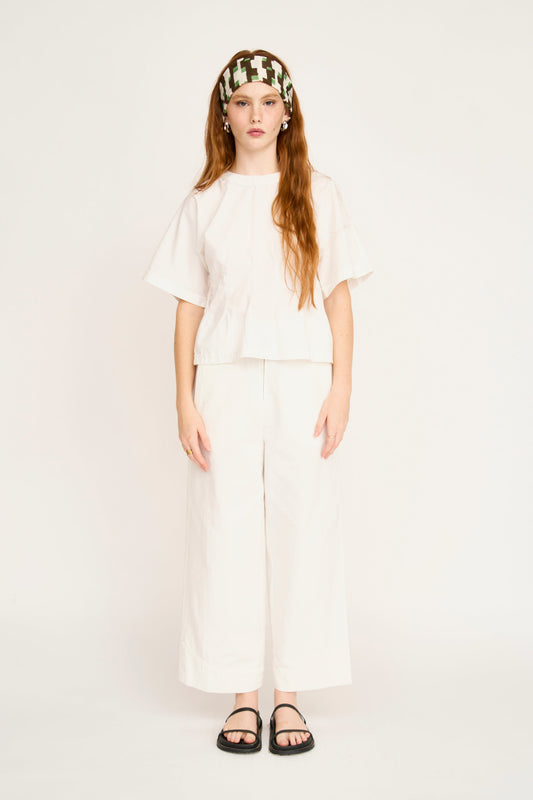 Model wearing white short-sleeve top with cream pants and patterned headband in studio setting