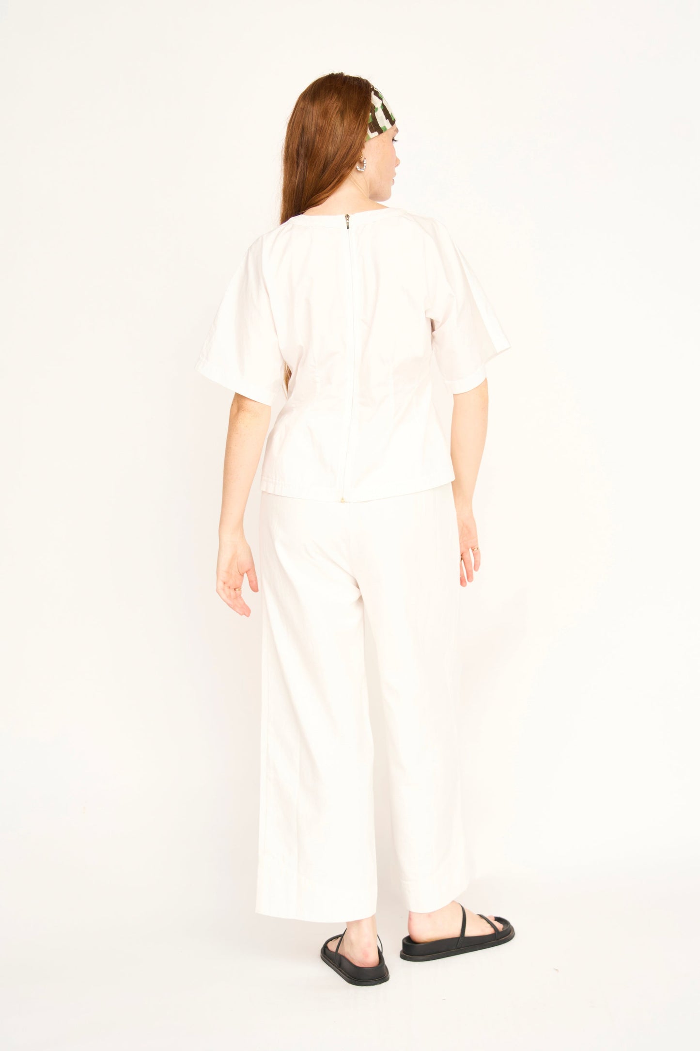 Back view of woman wearing white poplin top with matching pants and black sandals