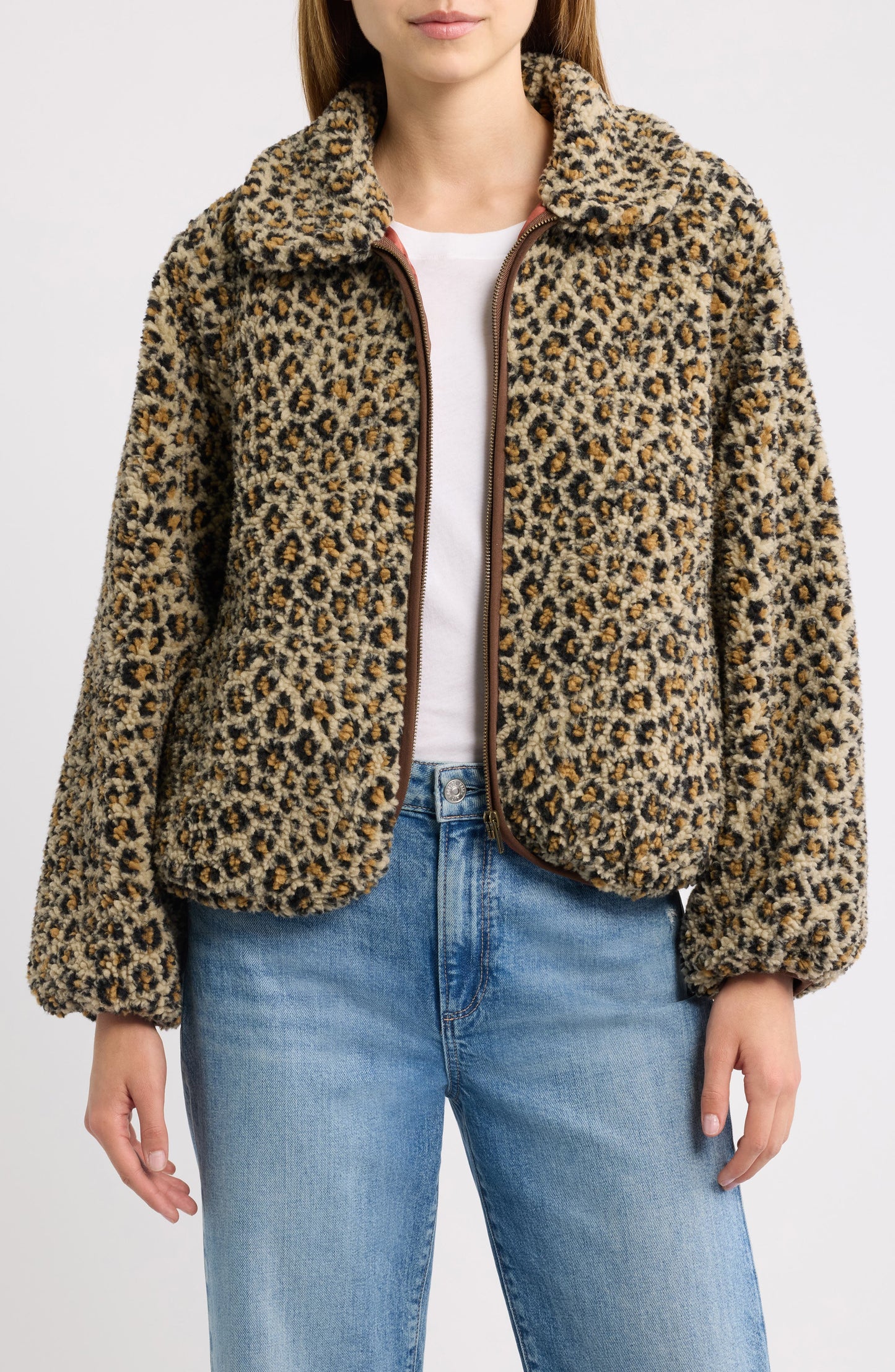 Woman wearing tan leopard print fleece zip-up jacket over white tee and jeans