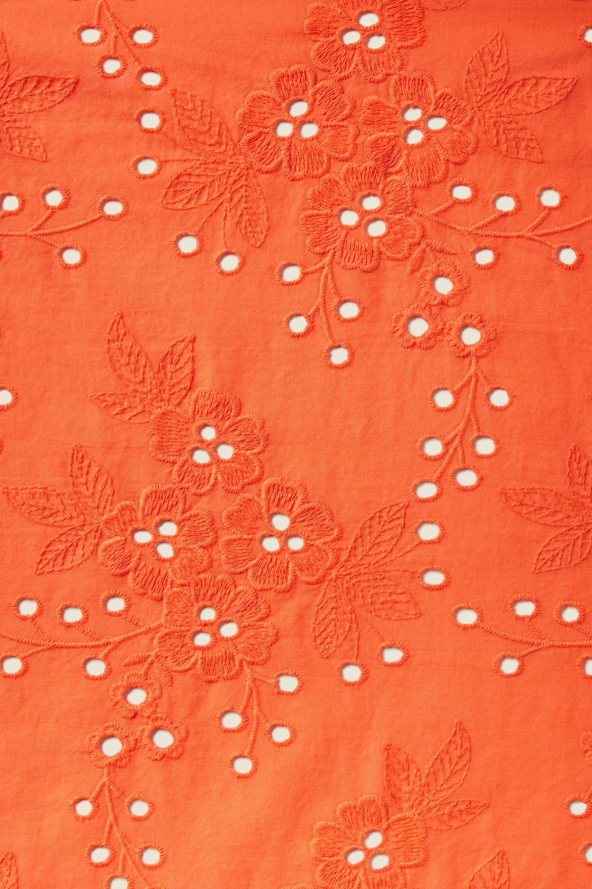 Close-up detail of coral orange eyelet fabric with embroidered floral pattern and cutout holes