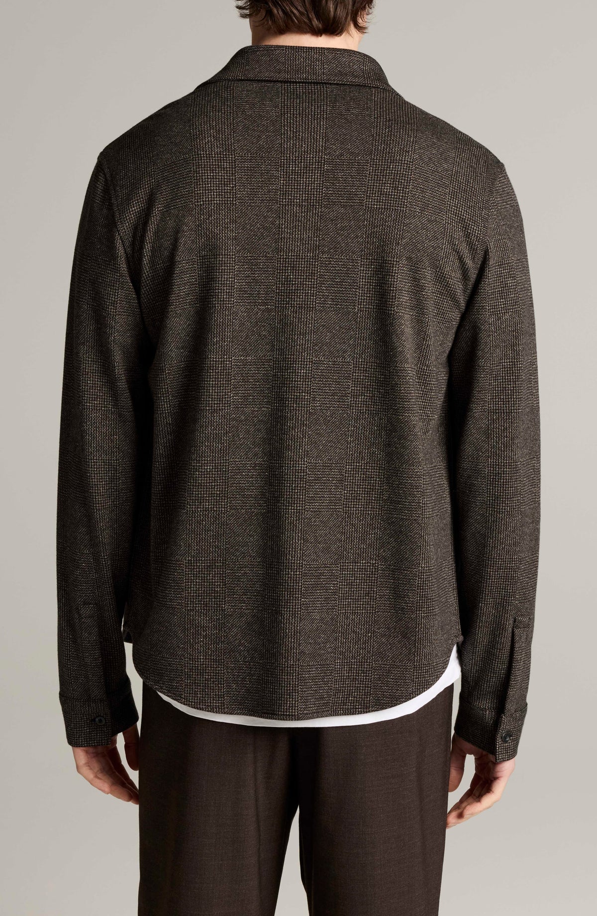 Back view of man wearing dark brown glen plaid long sleeve button-down shirt with white undershirt