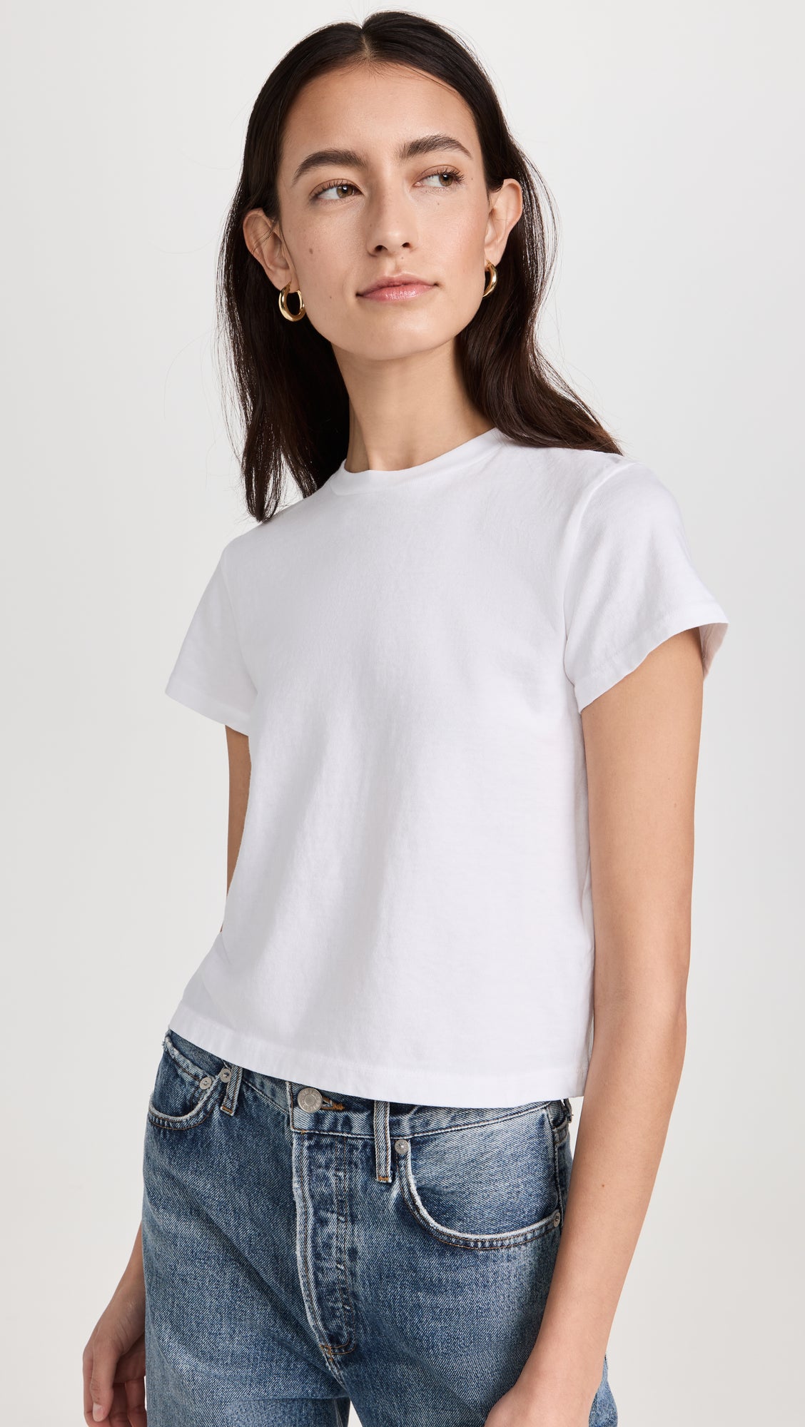 Woman wearing white short-sleeve crewneck t-shirt with blue jeans against neutral background