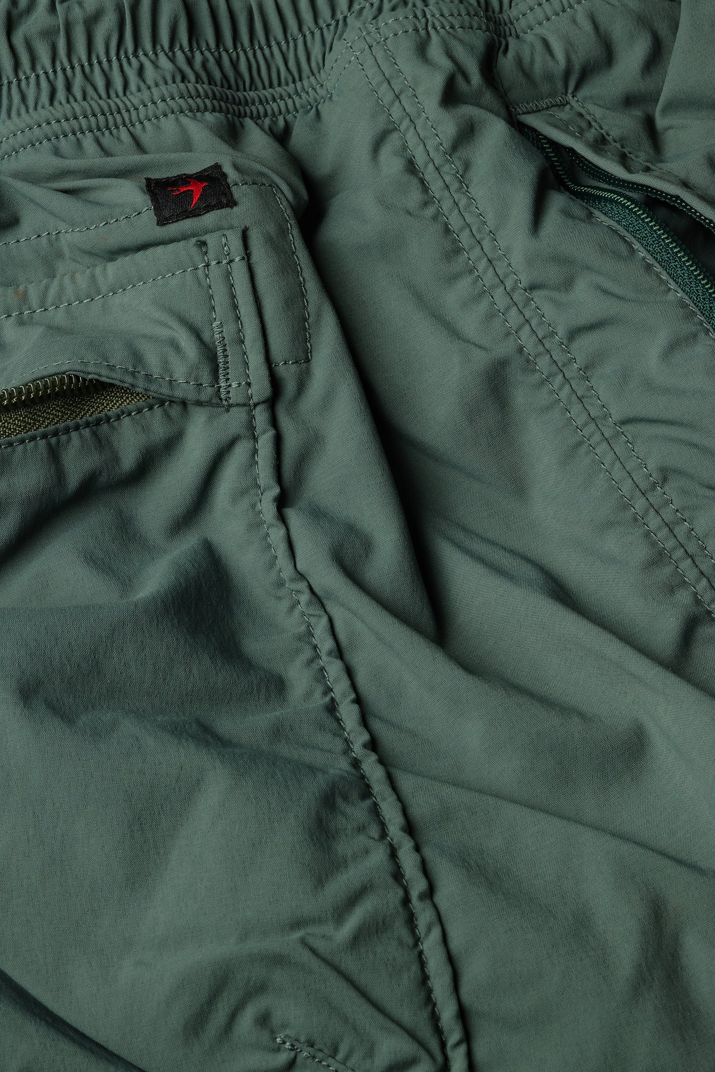 Relwen Airtex Hybrid shorts in olive green showing elastic waistband, zippered pockets, and detailed stitching construction.