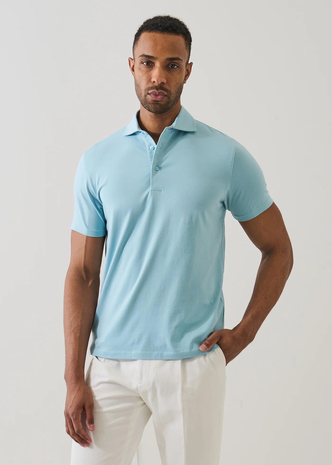 Man wearing Patrick Assaraf short-sleeve arctic blue pima cotton polo shirt with white pants in studio setting.