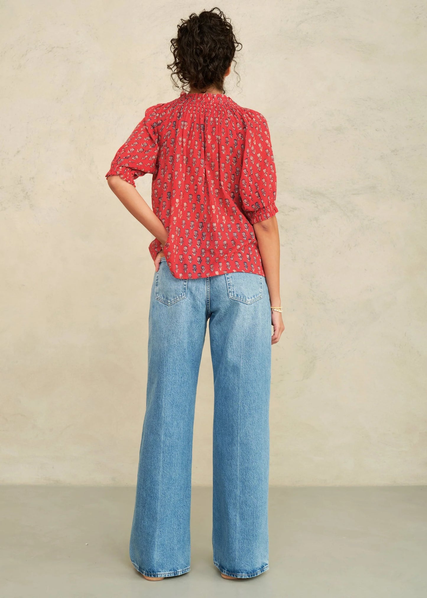 MABE Ari Print short sleeve top in red with small floral pattern, shown from back with wide-leg jeans.