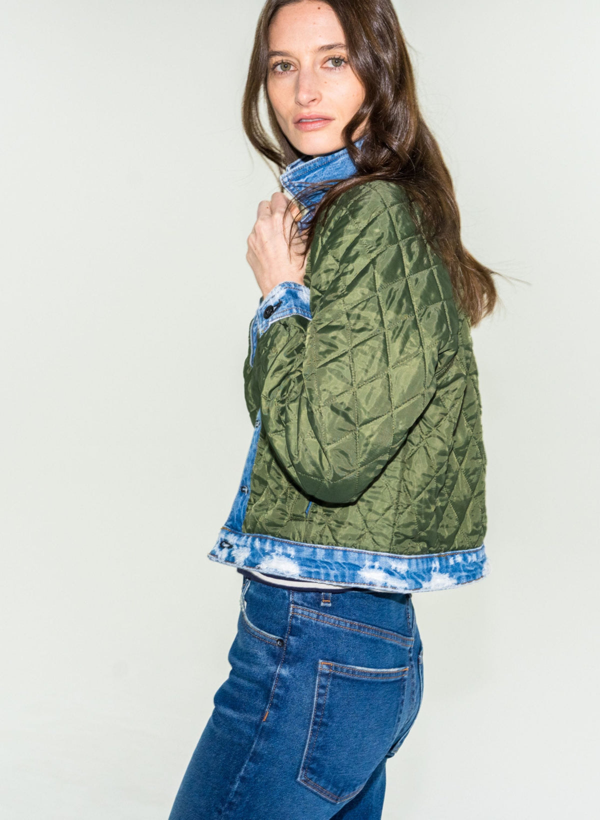 Model wearing olive green quilted liner jacket layered over tie-dye denim jacket with blue jeans