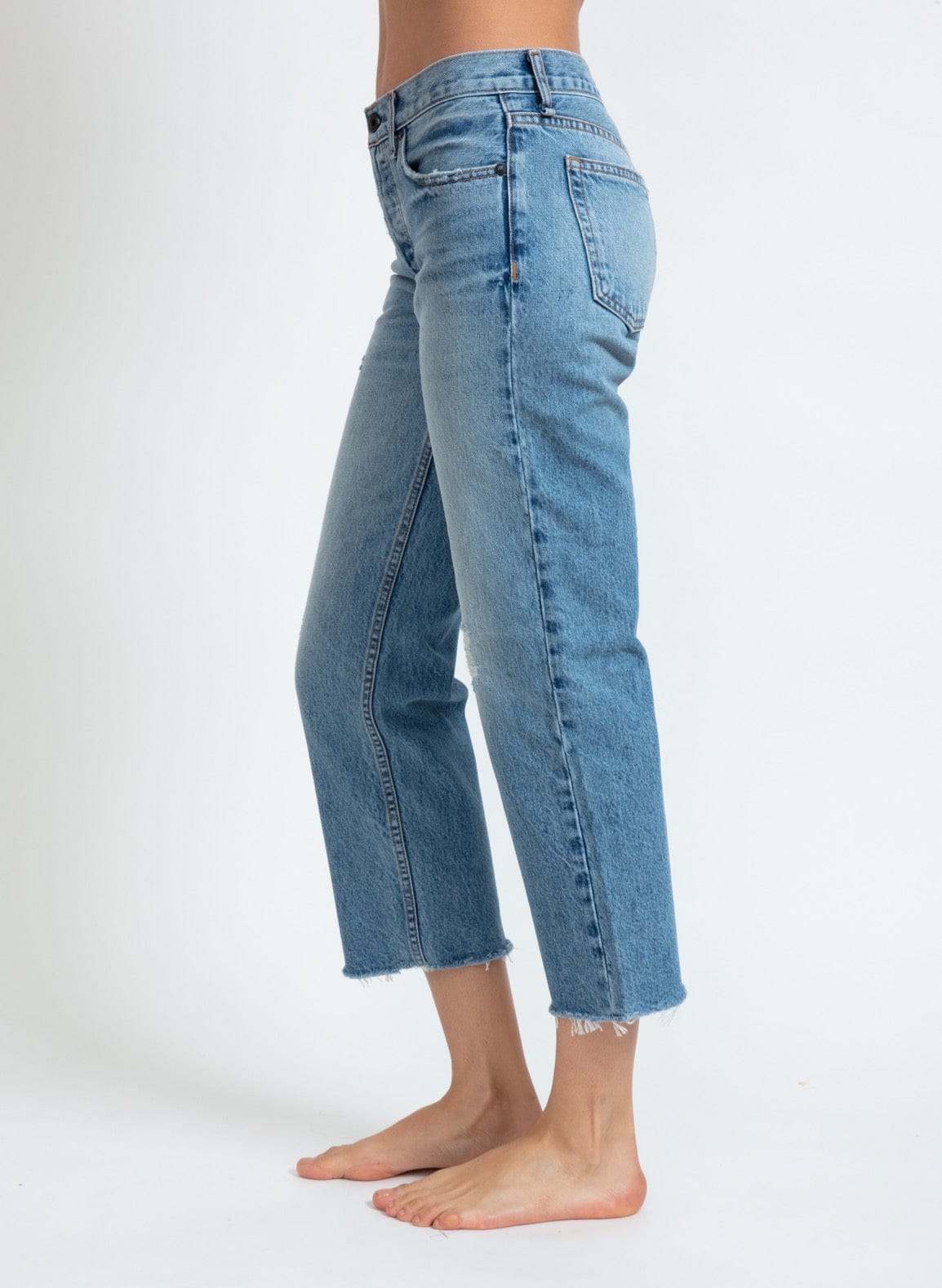 Side view of ASKK NY low rise straight leg cropped jeans in medium blue wash with raw hem