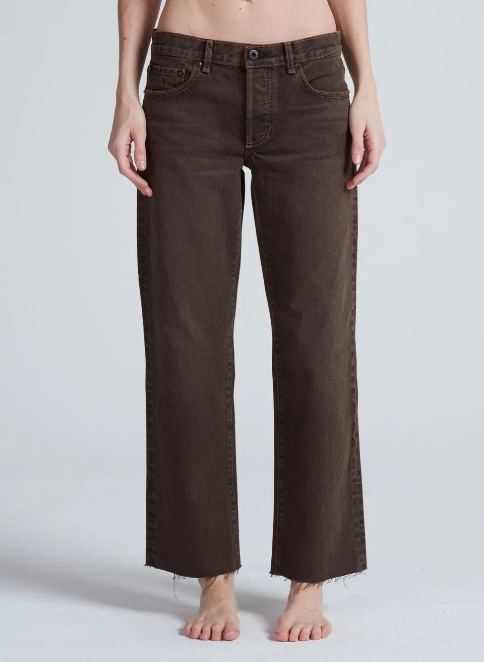 Model wearing ASKK NY low rise straight leg jeans in distressed brown with raw hem