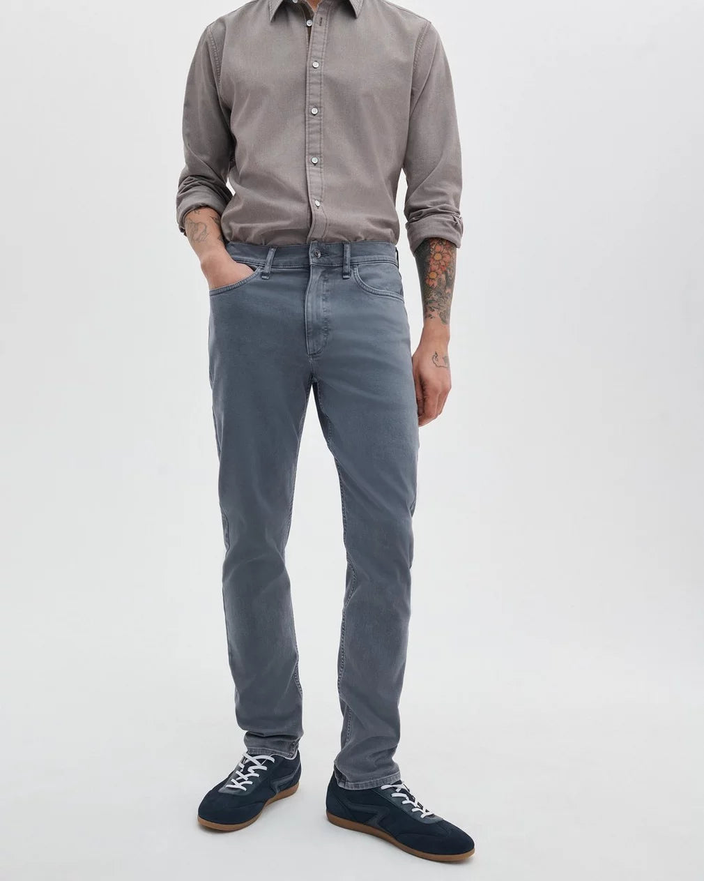 Man wearing Rag & Bone Fit 3 Airflex Bowery jeans in blue denim with gray button-up shirt and sneakers.