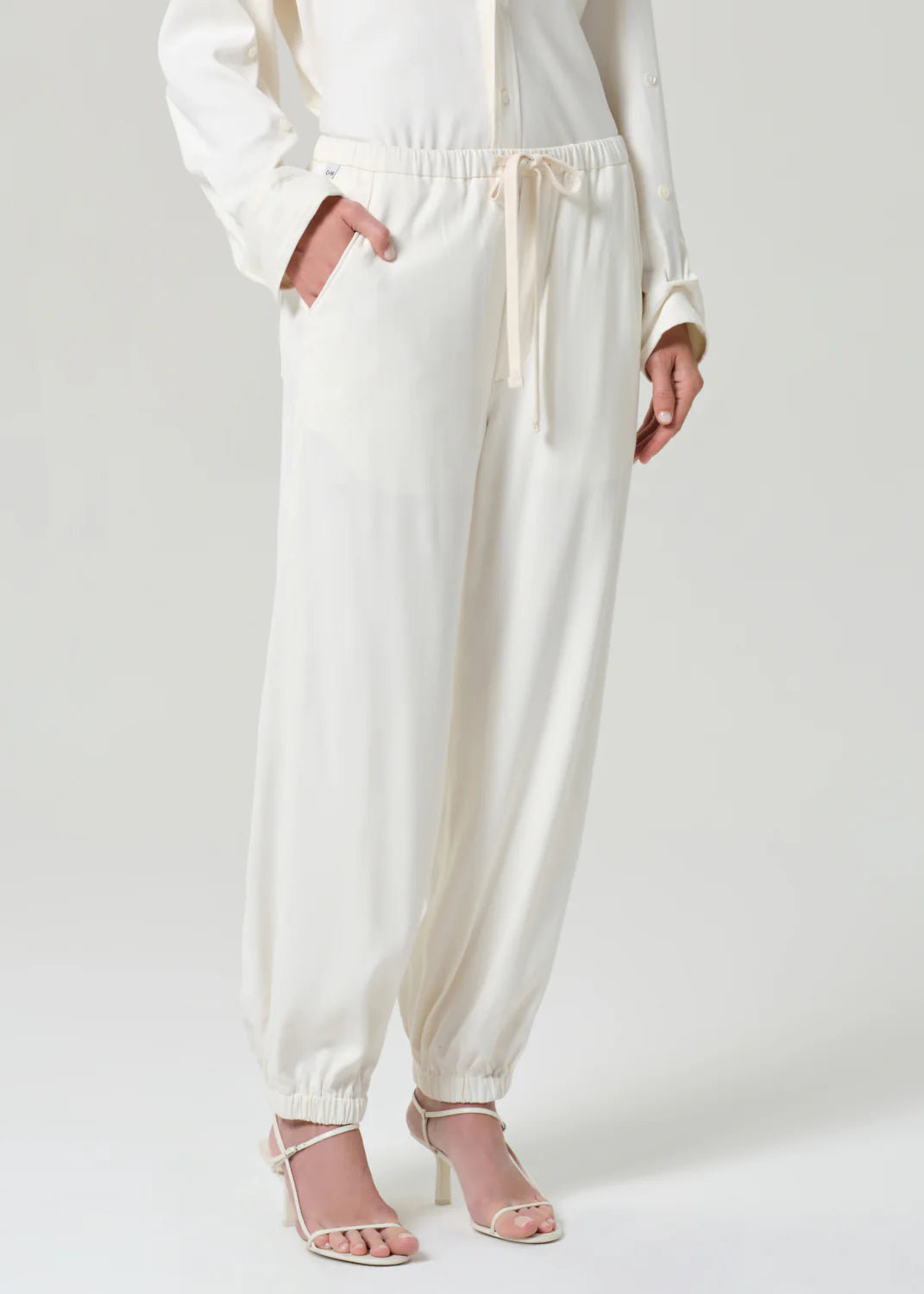 Citizens of Humanity white bubble pull-on jogger pants with elastic waistband and drawstring, worn with strappy heels