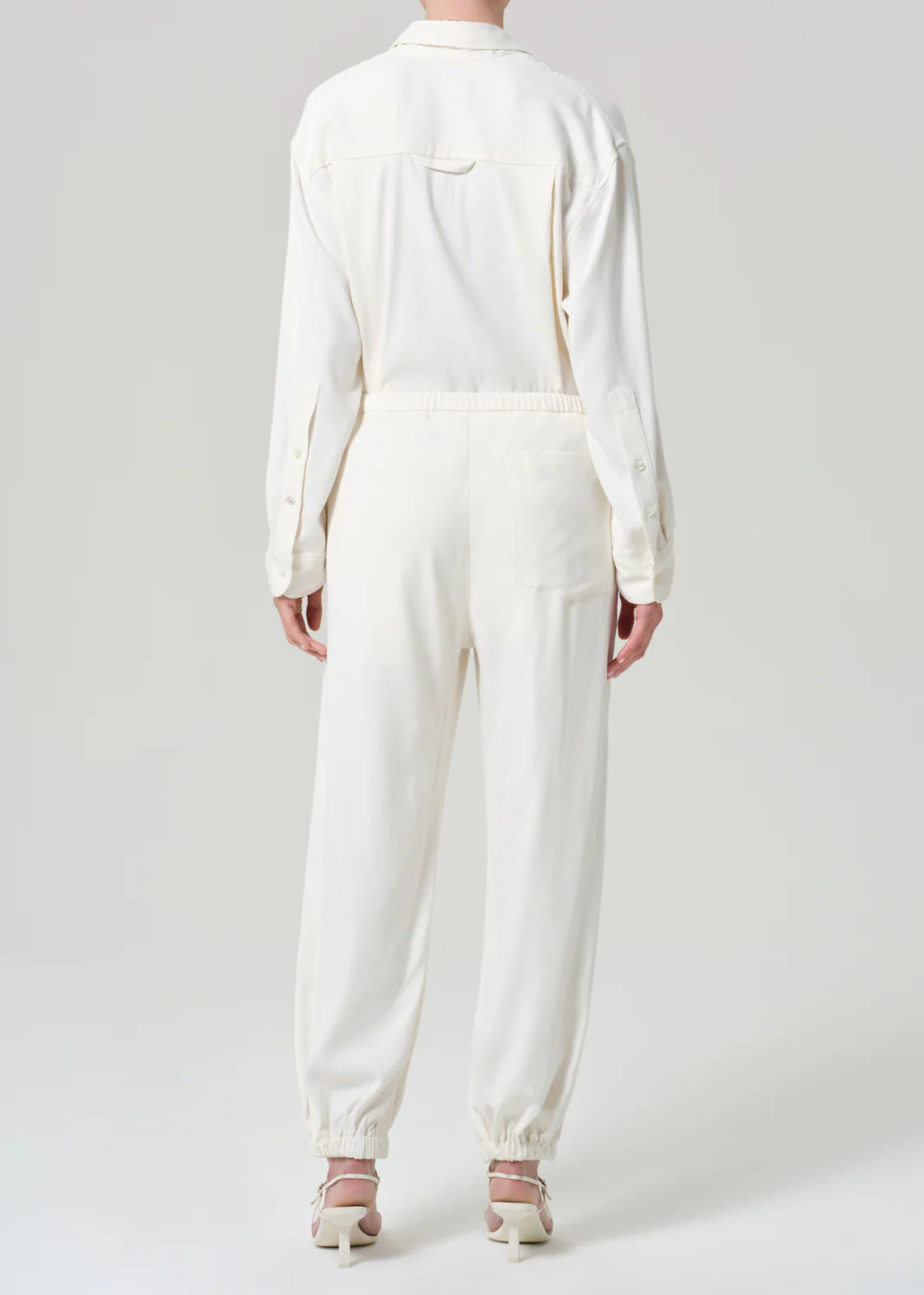 Citizens of Humanity white twill jumpsuit with elastic waist and cuffs, shown from behind on model wearing heels.