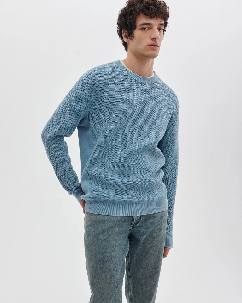 Man wearing Rag & Bone light blue crew neck sweater with jeans in casual styled pose.