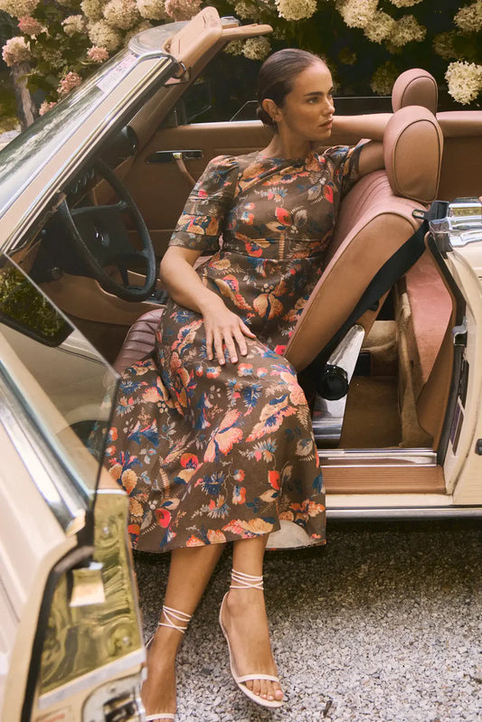 Hunter Bell Casey midi dress in olive floral print featuring short sleeves and fitted silhouette on model in convertible car.