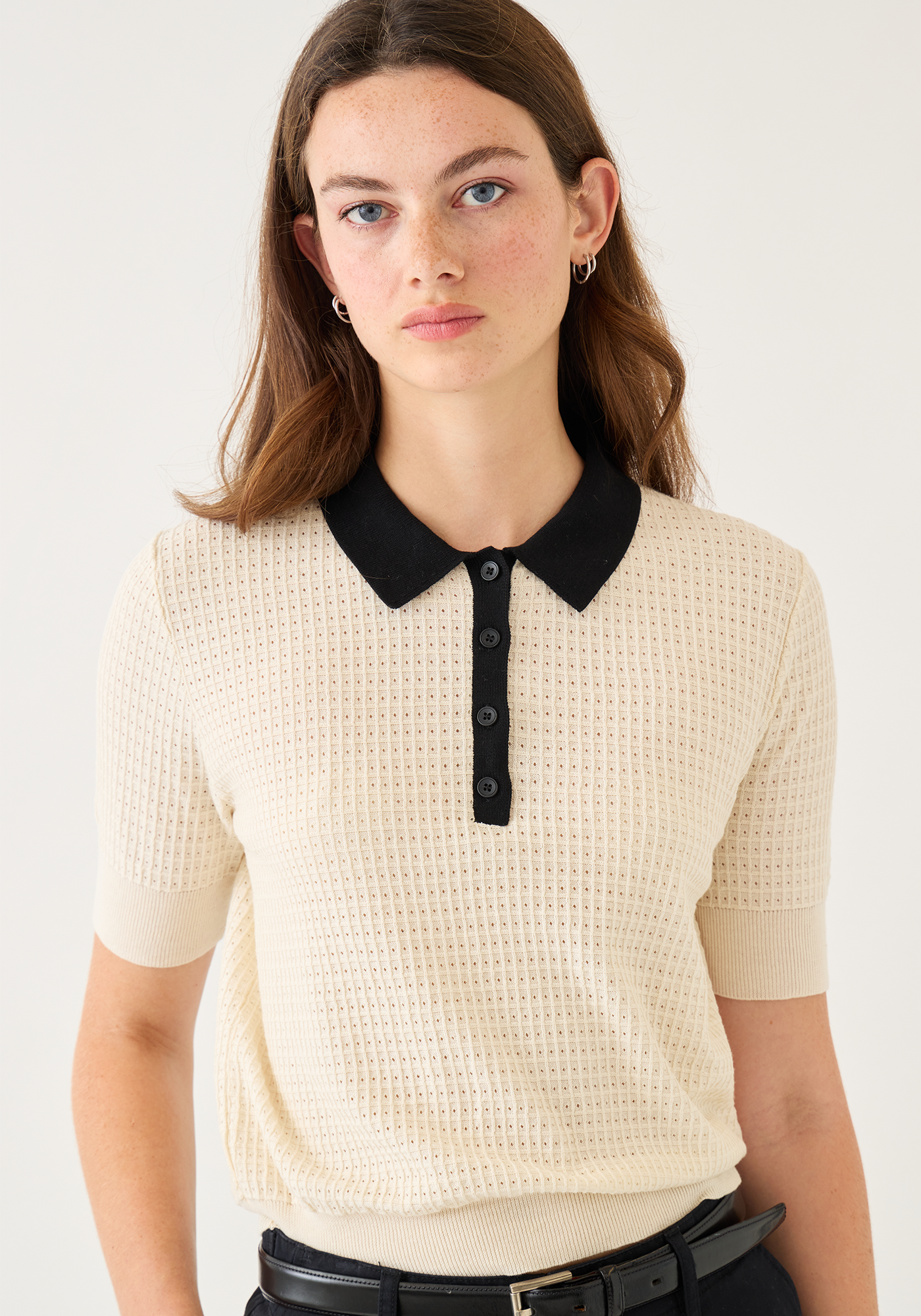 Woman wearing cream waffle knit polo top with black collar and button placket