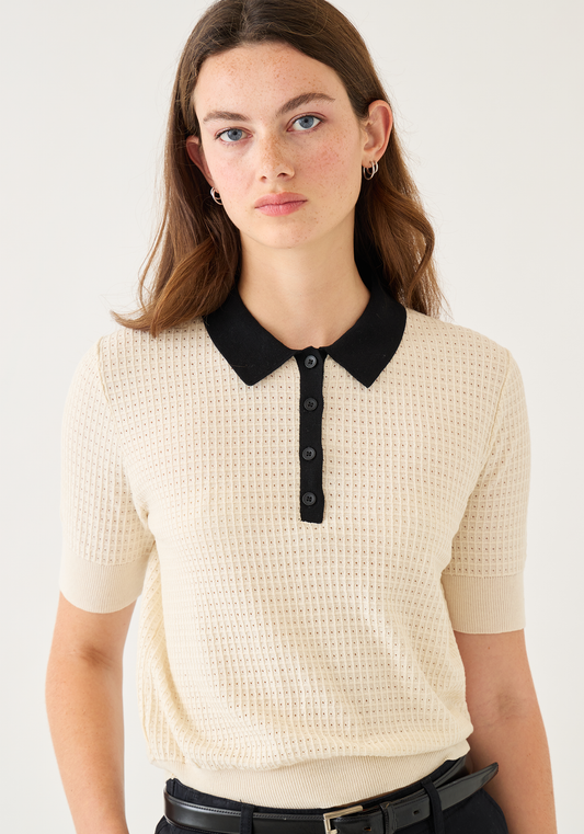 Woman wearing cream waffle knit polo top with black collar and button placket