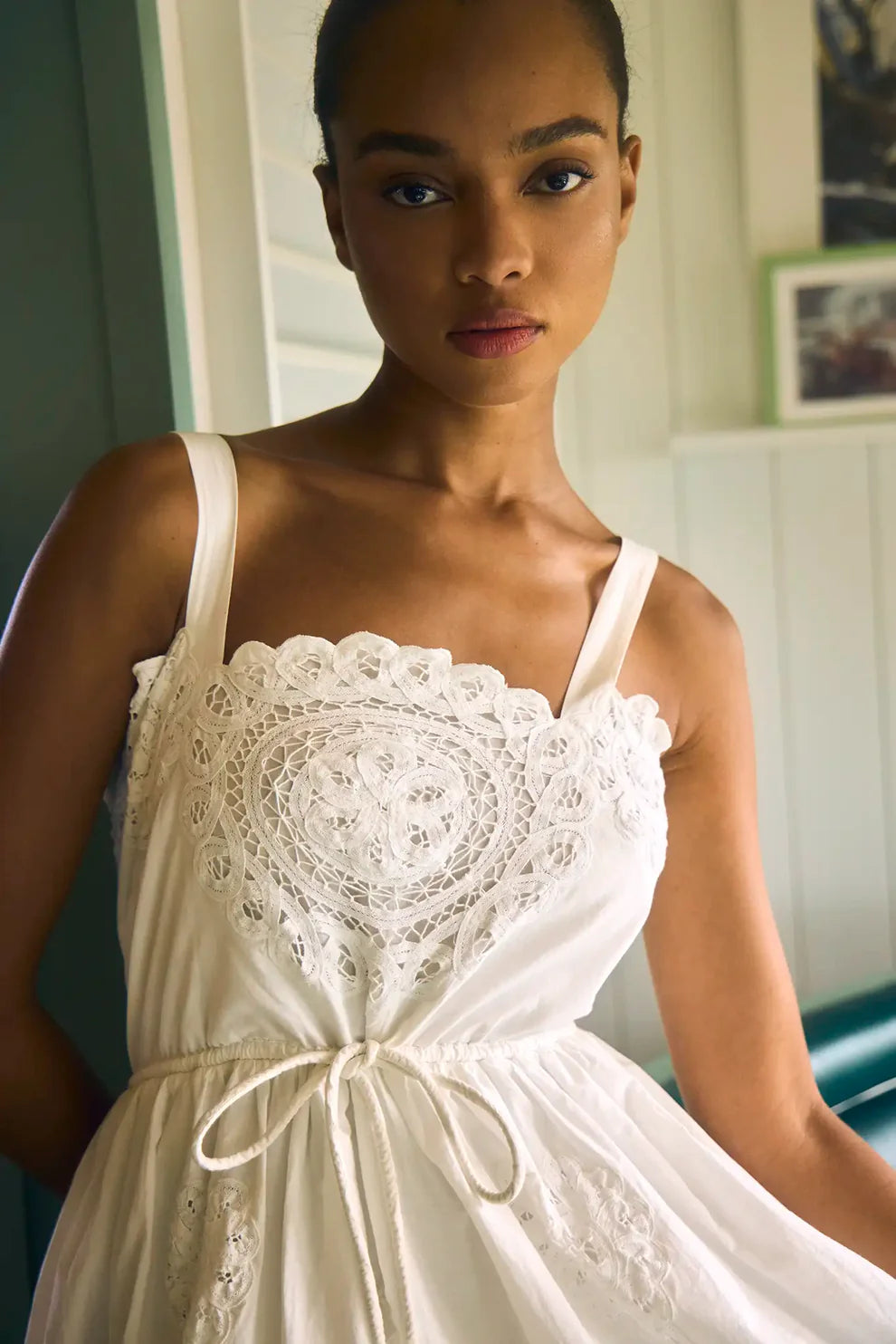 Hunter Bell Cosette white dress with intricate lace bodice detail and tie waist, modeled indoors.