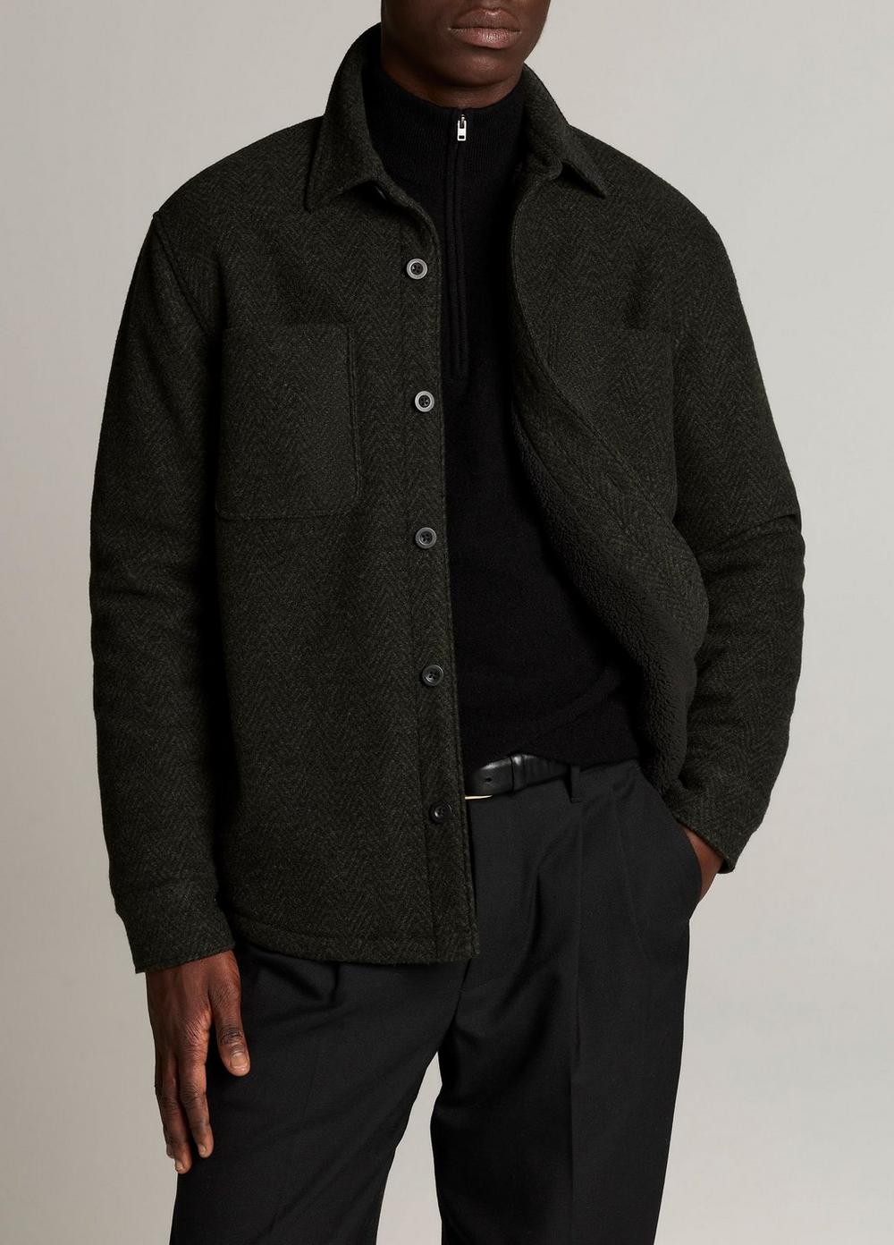 Male model wearing dark green herringbone sherpa-lined shirt jacket over black half-zip