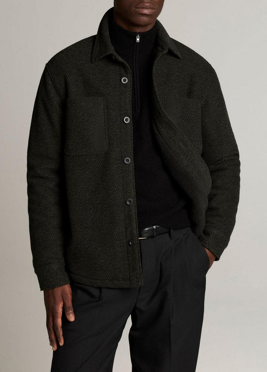 Male model wearing dark green herringbone sherpa-lined shirt jacket over black half-zip