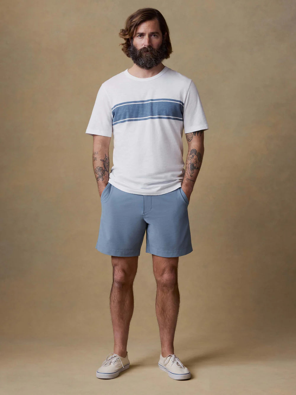 Man wearing Faherty striped t-shirt and blue All Day Shorts 7" with white sneakers against neutral background.