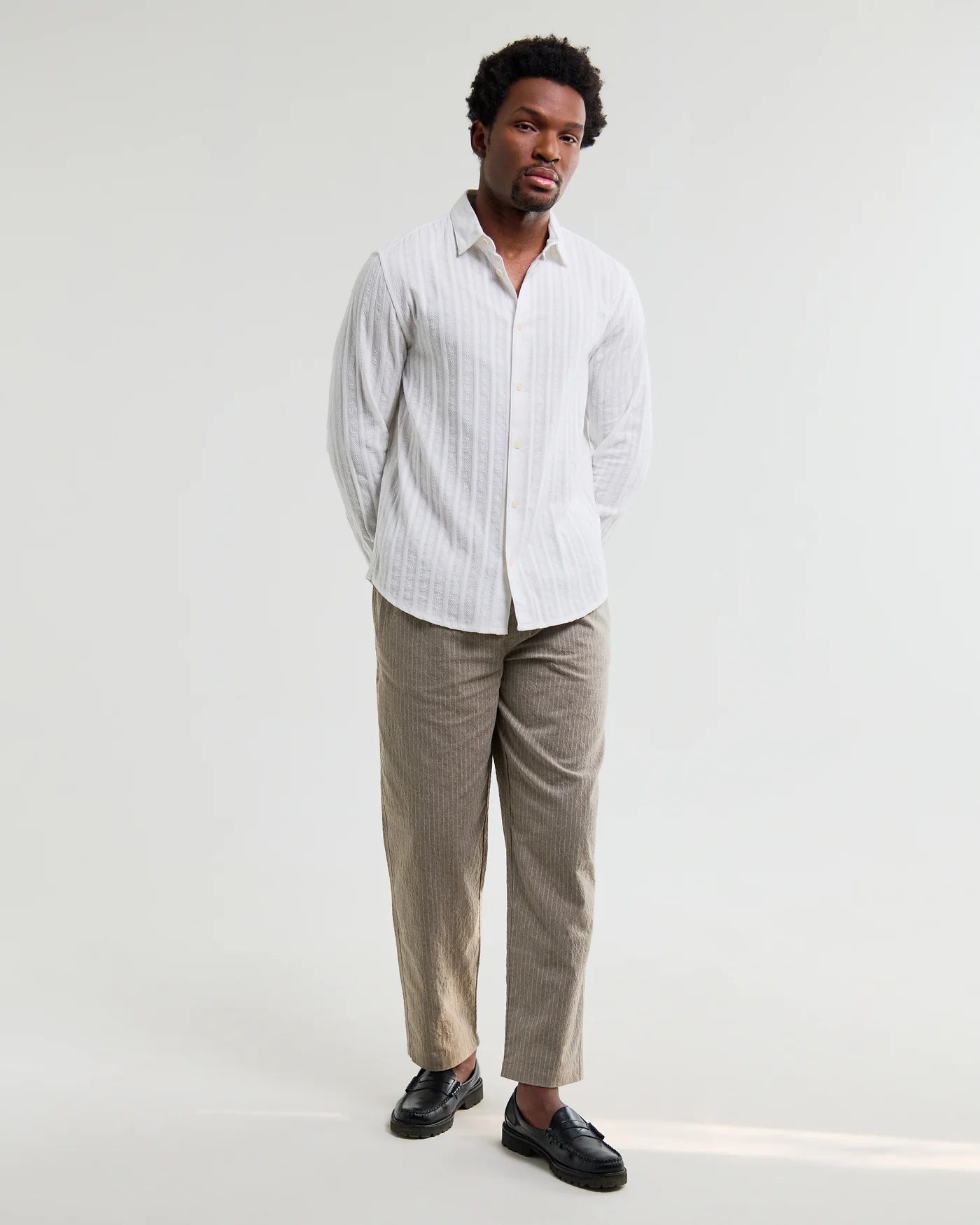 Man wearing Wax London Dartford long sleeve dobby stripe white shirt with beige trousers and black loafers.