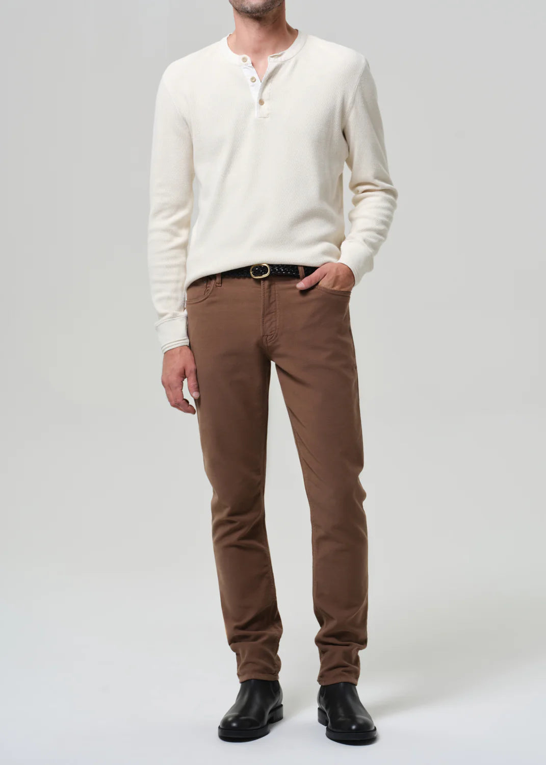 Man wearing cream henley shirt and brown Citizens of Humanity Adler jeans in French Terry with black leather shoes.