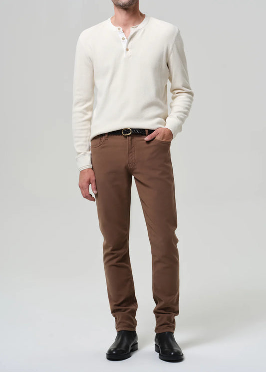 Man wearing cream henley shirt and brown Citizens of Humanity Adler jeans in French Terry with black leather shoes.