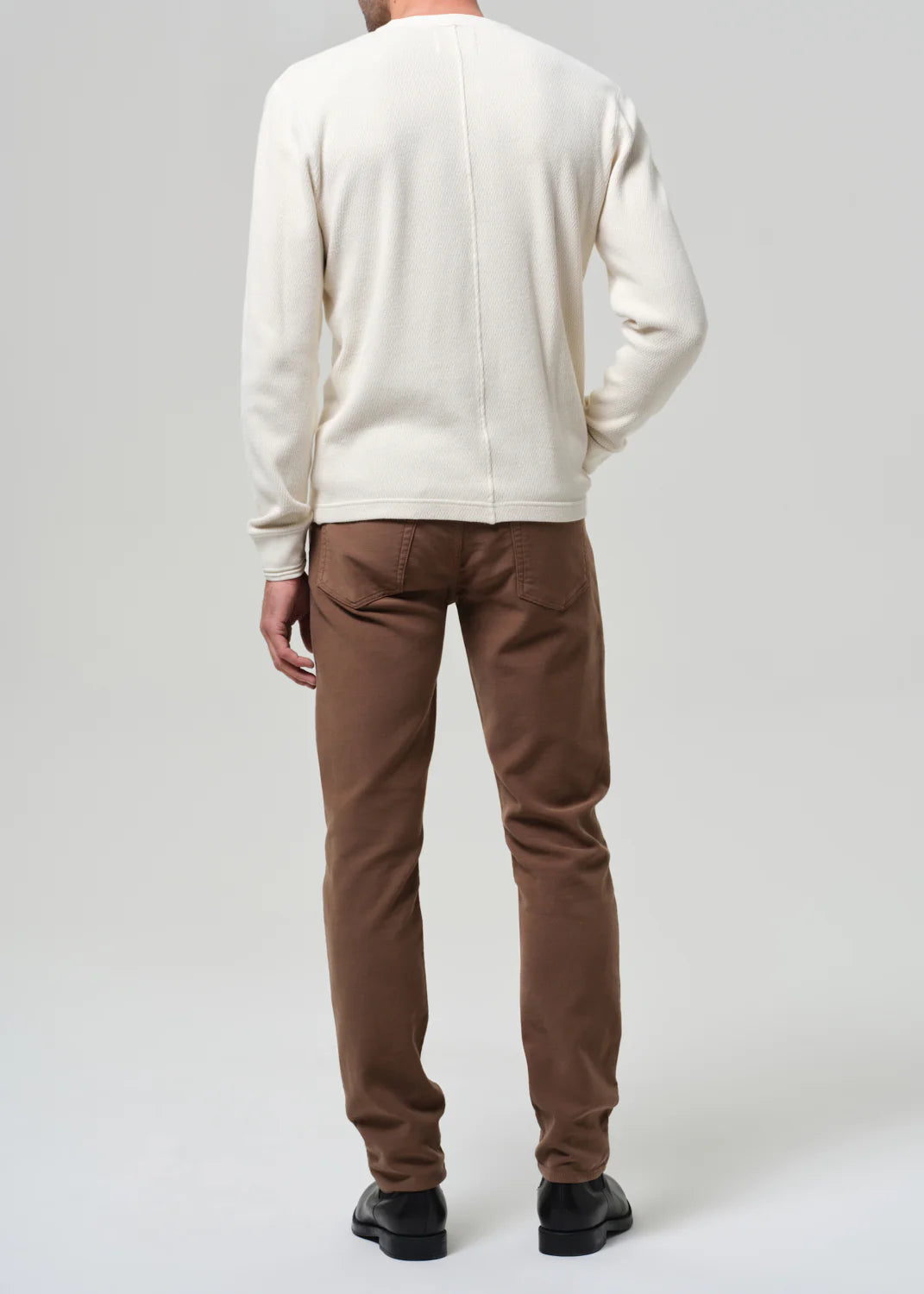 Back view of man wearing cream sweatshirt and brown Citizens of Humanity Adler jeans with black shoes