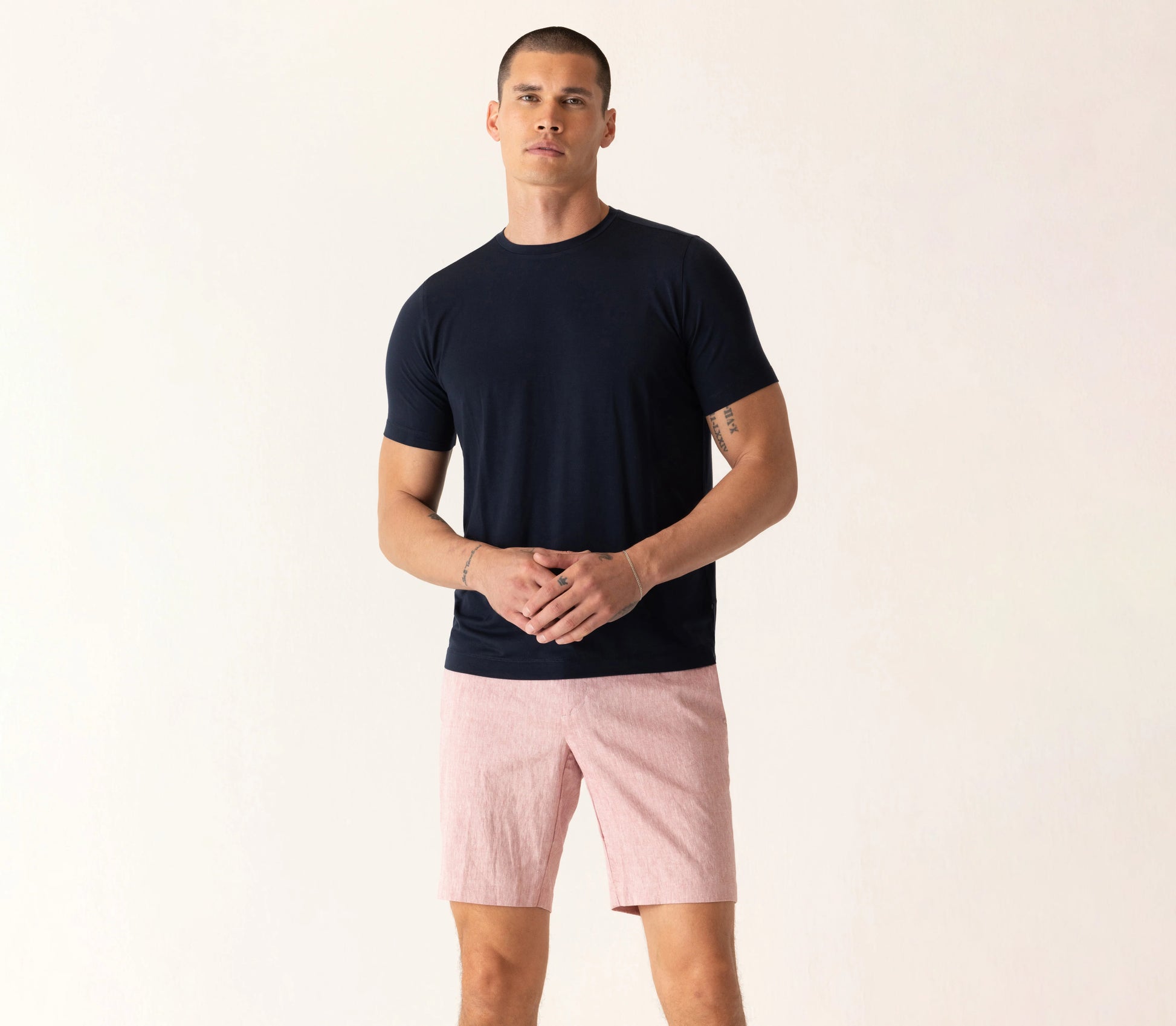 Man wearing a black crew neck t-shirt and pink linen shorts standing against a neutral background