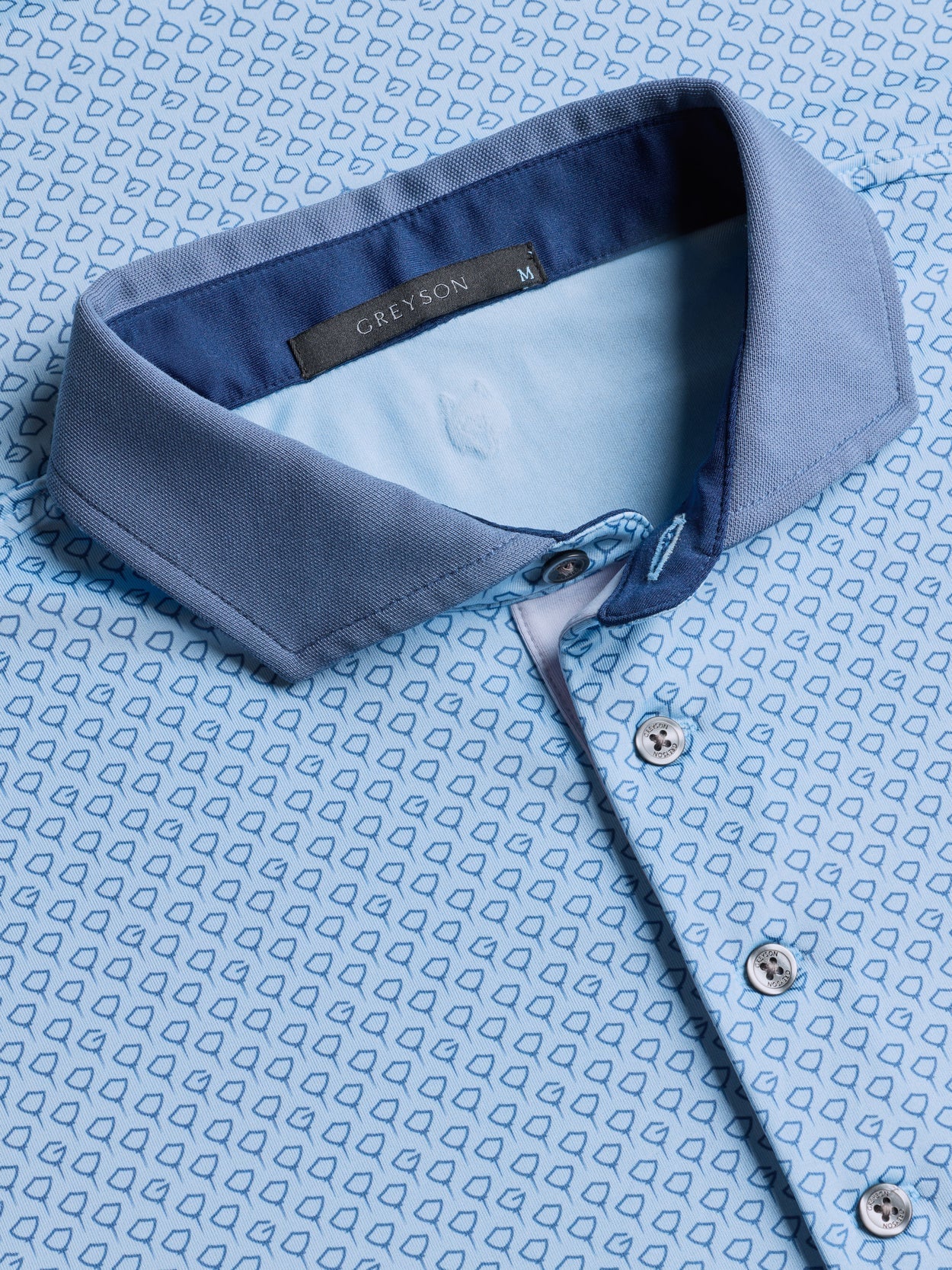 Greyson Drifter Polo in light blue with small geometric pattern, showing collar detail and button placket.