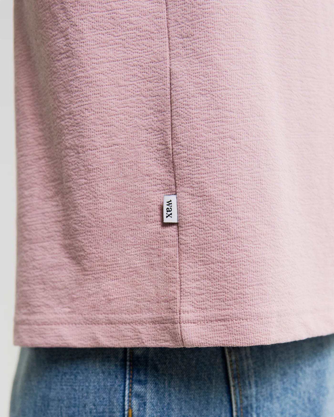 Wax London Dean short sleeve t-shirt in dusty pink showing bottom hem with brand label detail over jeans