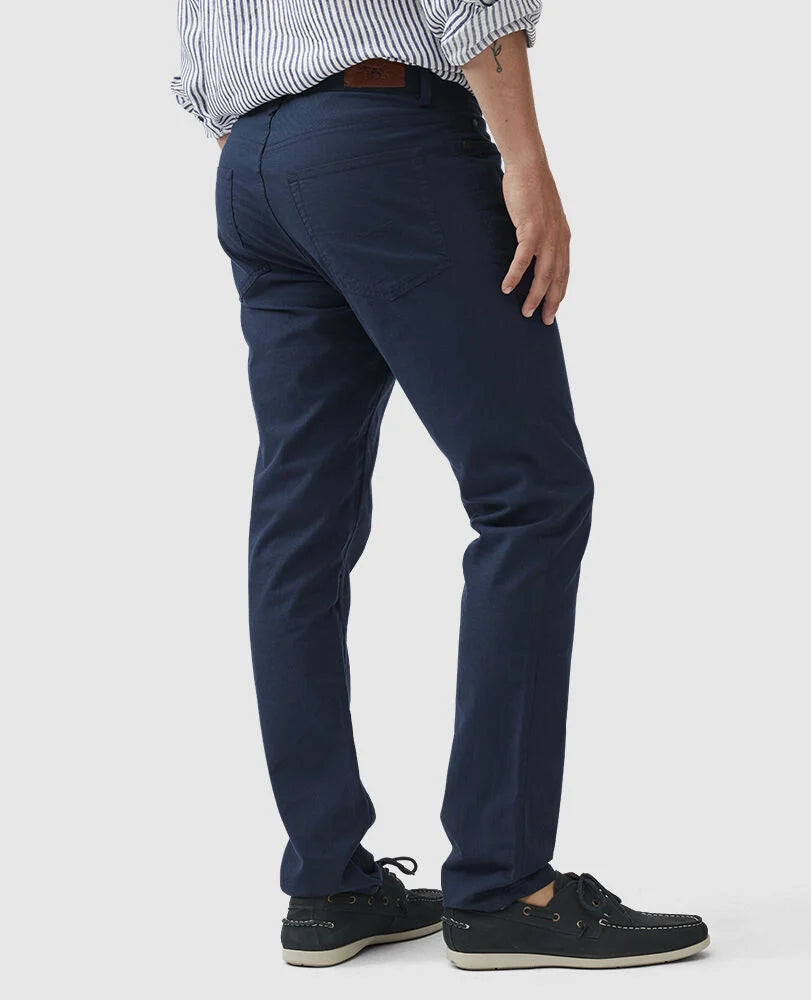 Man wearing Rodd & Gunn navy five-pocket pants with striped shirt and boat shoes, rear three-quarter view.