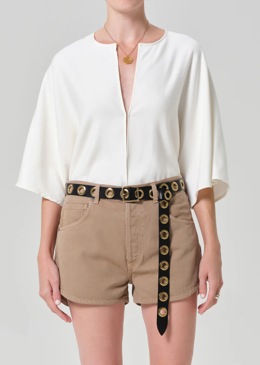 Woman wearing Citizens of Humanity white button-up shirt with rolled sleeves, styled with beige shorts and studded belt.